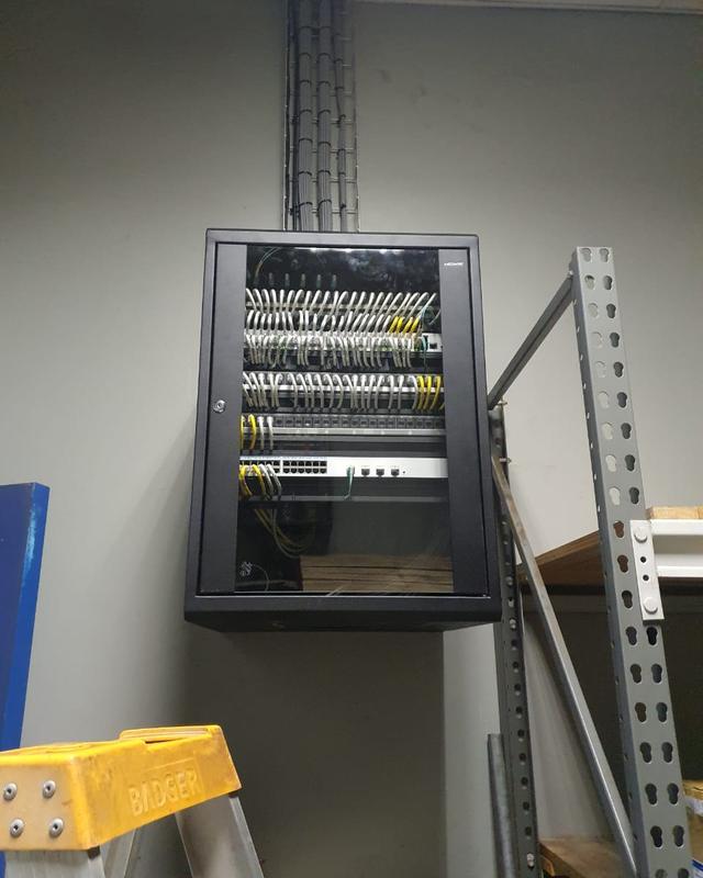 A wall-mounted network cabinet with patched cables, fed by a cable ladder from the ceiling